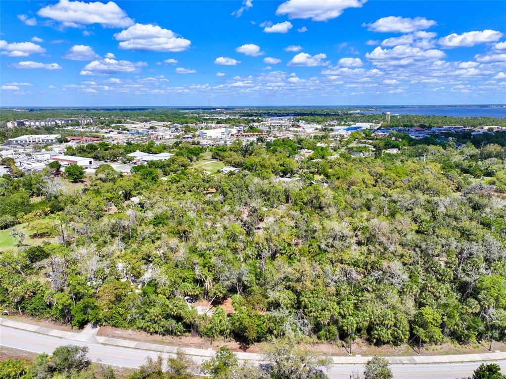 An aerial view shows a large, wooded lot bordering a road with a town beyond — 22901 BAYSHORE ROAD, PUNTA GORDA, FL