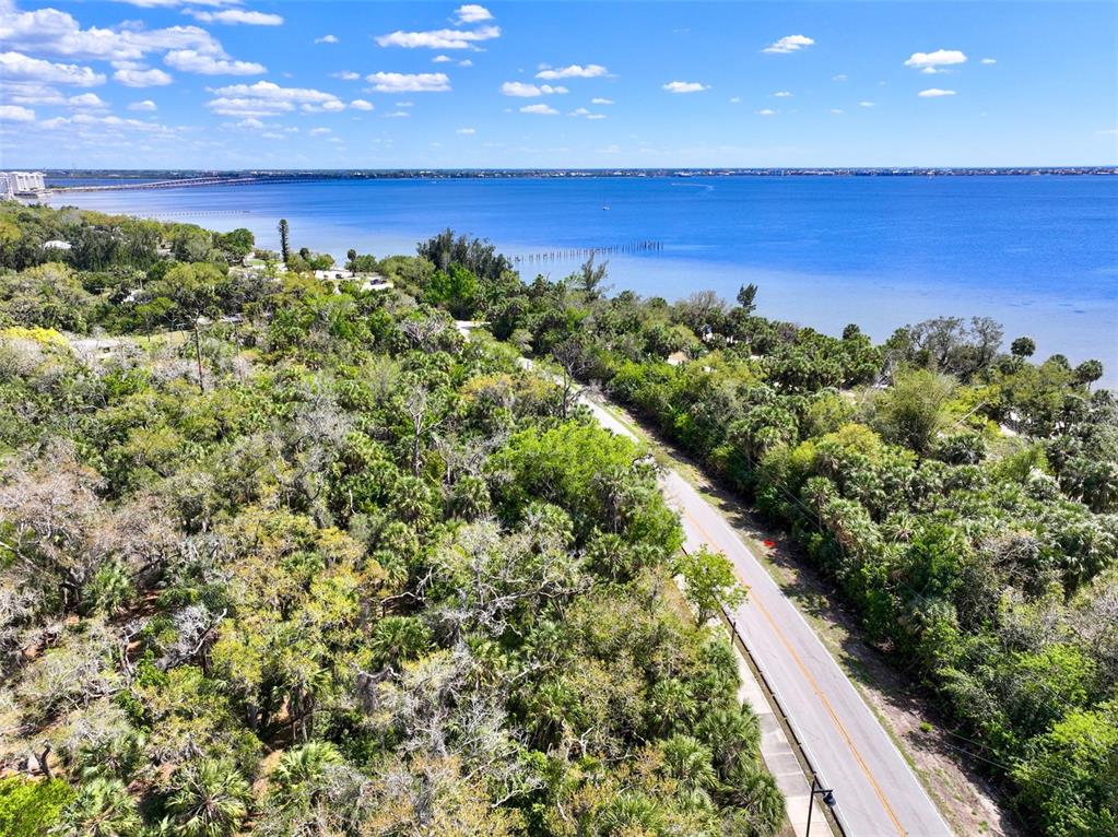 An aerial view shows a road winding through dense trees alongside a large blue bay — 22901 BAYSHORE ROAD, PUNTA GORDA, FL