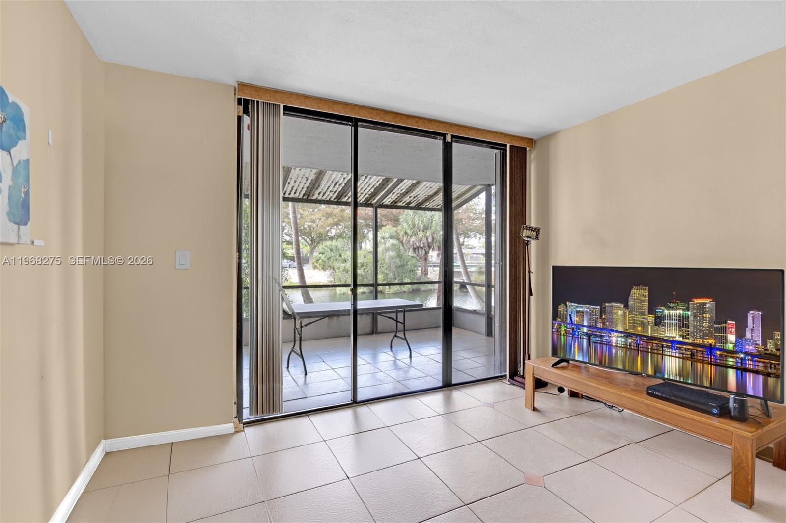 A living room with tile flooring features a sliding glass door leading to a screened patio — 8305 SW 152nd Ave # 107, Miami FL 33193, MIAMI, FL