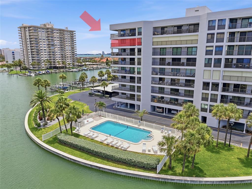 An aerial view shows a multi-story apartment building with balconies, a swimming pool, and a marina — 1651 SAND KEY ESTATES COURT UNIT 78, CLEARWATER BEACH, FL