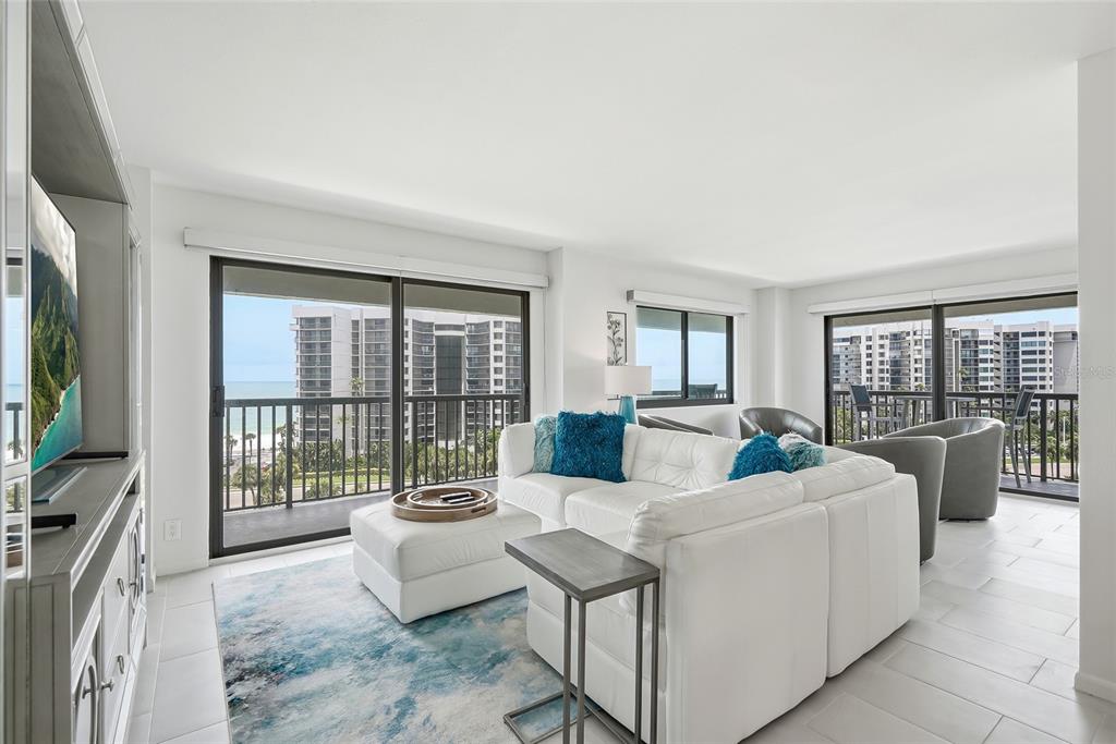 A bright living room features a white sectional sofa, blue accents, and balcony ocean views — 1651 SAND KEY ESTATES COURT UNIT 78, CLEARWATER BEACH, FL