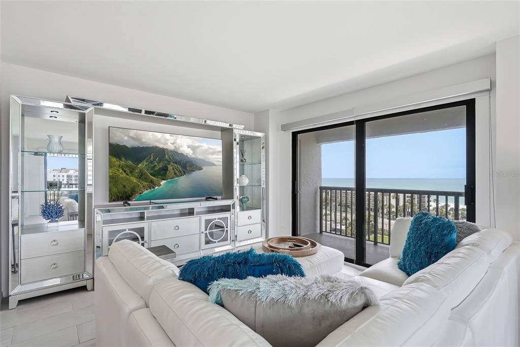A living room features a white sectional sofa, mirrored entertainment center, and a balcony overlooking the ocean — 1651 SAND KEY ESTATES COURT UNIT 78, CLEARWATER BEACH, FL