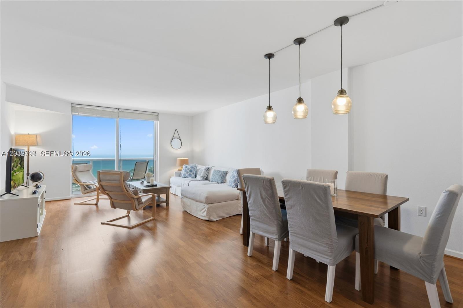 A living and dining area features wood flooring, white walls, and a view of the ocean — 10275 Collins Ave # 718, Bal Harbour FL 33154, BAL HARBOUR, FL