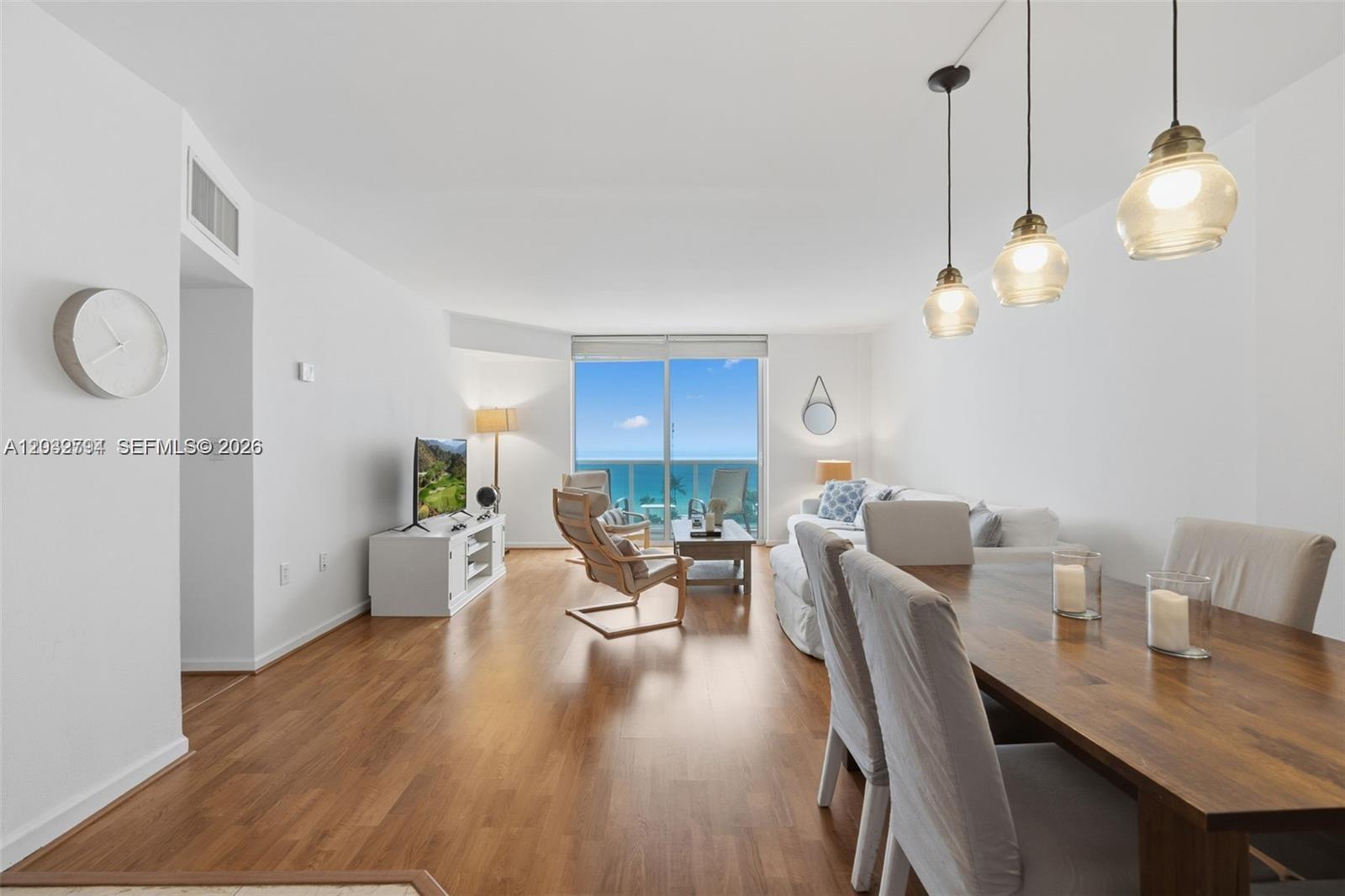 An open-concept living and dining area features hardwood floors, modern lighting, and ocean views — 10275 Collins Ave # 718, Bal Harbour FL 33154, BAL HARBOUR, FL