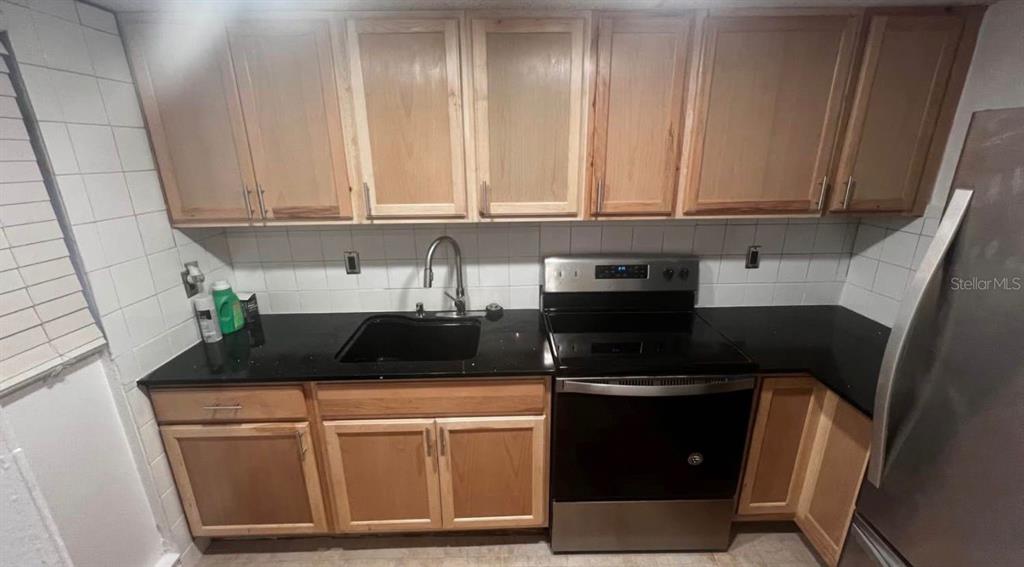 A kitchen features light wood cabinets, black countertops, a stainless steel stove, and white tiles — 707 SW 75TH ST UNIT 109, GAINESVILLE, FL
