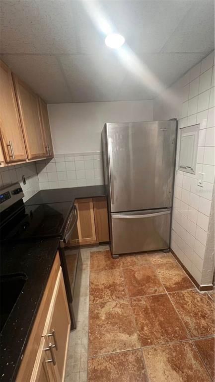 A kitchen features light wood cabinets, black countertops, a stainless steel refrigerator, and tiled flooring — 707 SW 75TH ST UNIT 109, GAINESVILLE, FL