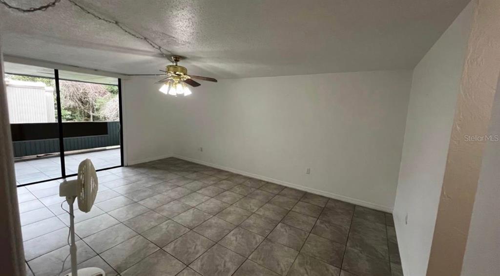 A living room features light-colored tile flooring, white walls, a ceiling fan, and sliding glass doors — 707 SW 75TH ST UNIT 109, GAINESVILLE, FL