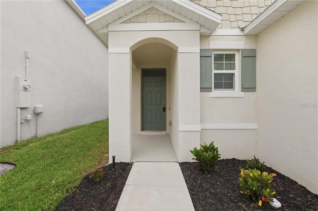 A beige house exterior features a covered entryway, a green front door, and green shutters — 1749 SHADOW TRACE WAY, DELAND, FL