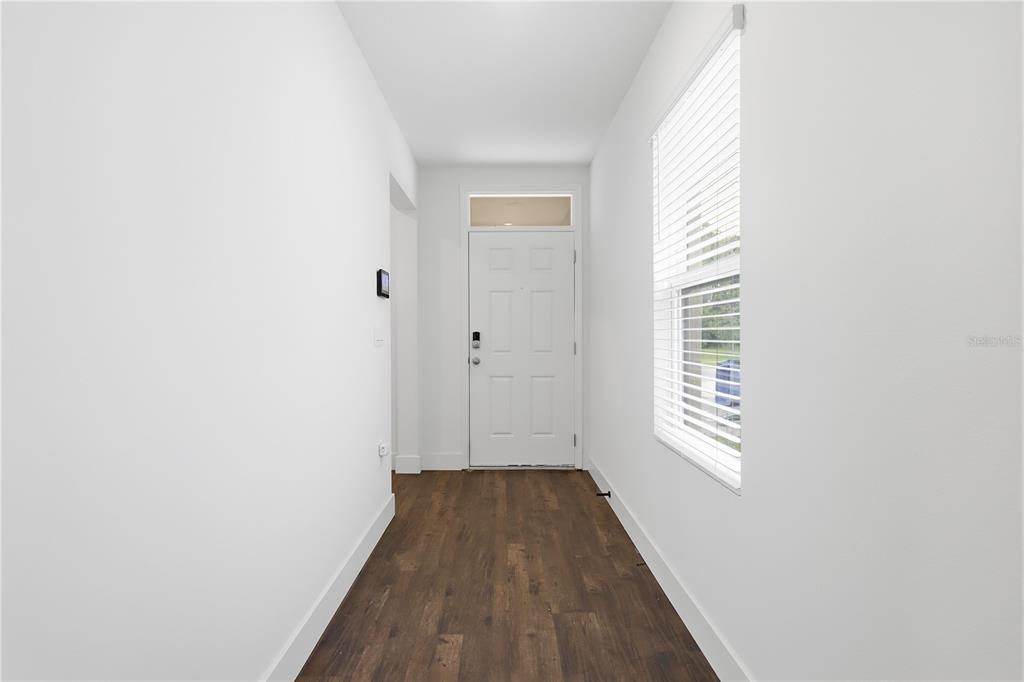 A bright entryway features white walls, dark wood-look flooring, and a white front door — 1749 SHADOW TRACE WAY, DELAND, FL