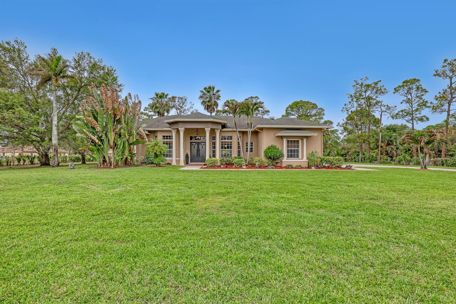 A single-story tan house with columns and a large front lawn under a blue sky — 14042 88th Place N, FL 33470, FL