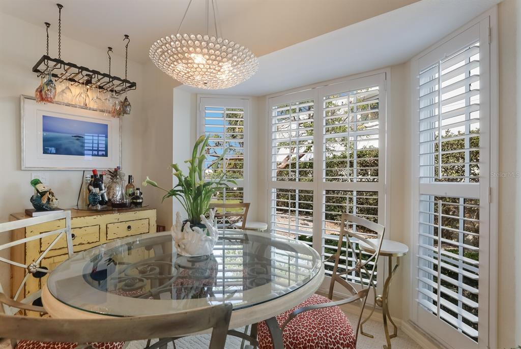 A dining area features a glass-topped table, a crystal chandelier, and white plantation window shutters — 5856 GASPARILLA ROAD UNIT M31, BOCA GRANDE, FL