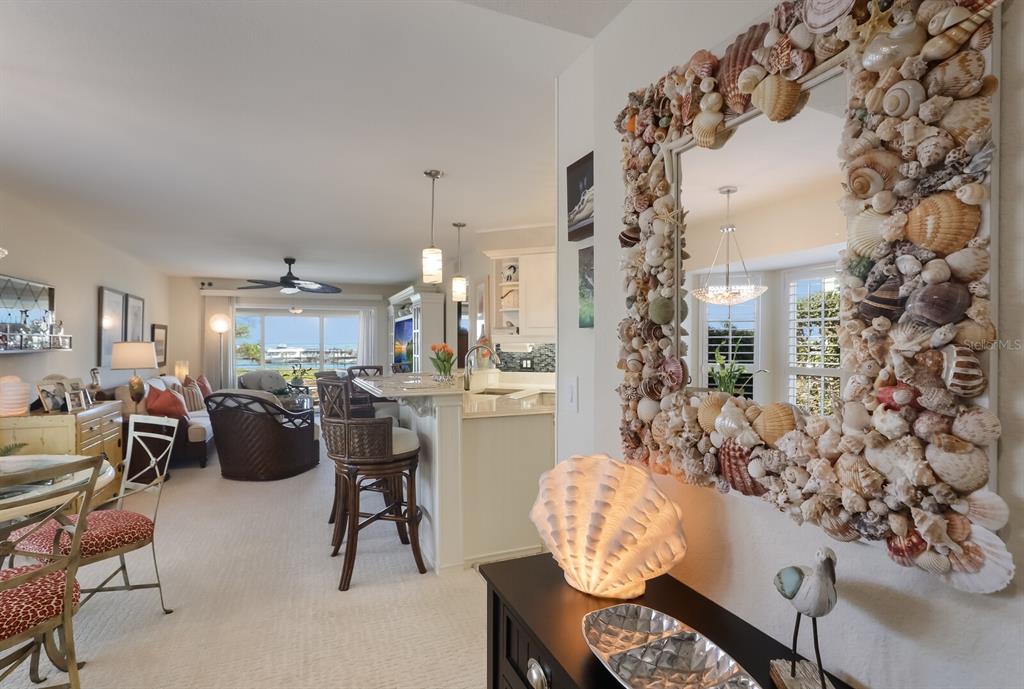 A living room and kitchen area features a seashell-framed mirror and a water view — 5856 GASPARILLA ROAD UNIT M31, BOCA GRANDE, FL