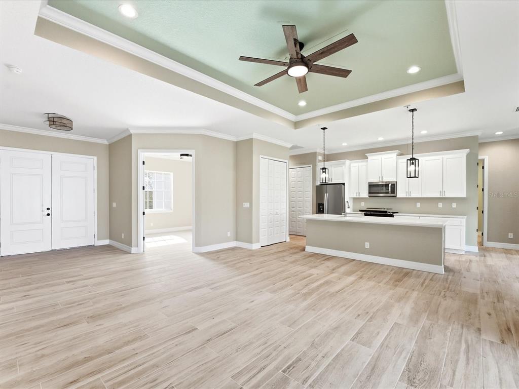 An open-concept kitchen and living area featuring a tray ceiling, light wood flooring, and white cabinetry — 13364 RAYBURN LANE, PORT CHARLOTTE, FL