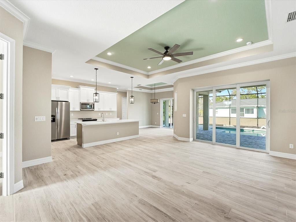 An open-concept kitchen and living area with light wood floors, a tray ceiling, and pool view — 13364 RAYBURN LANE, PORT CHARLOTTE, FL