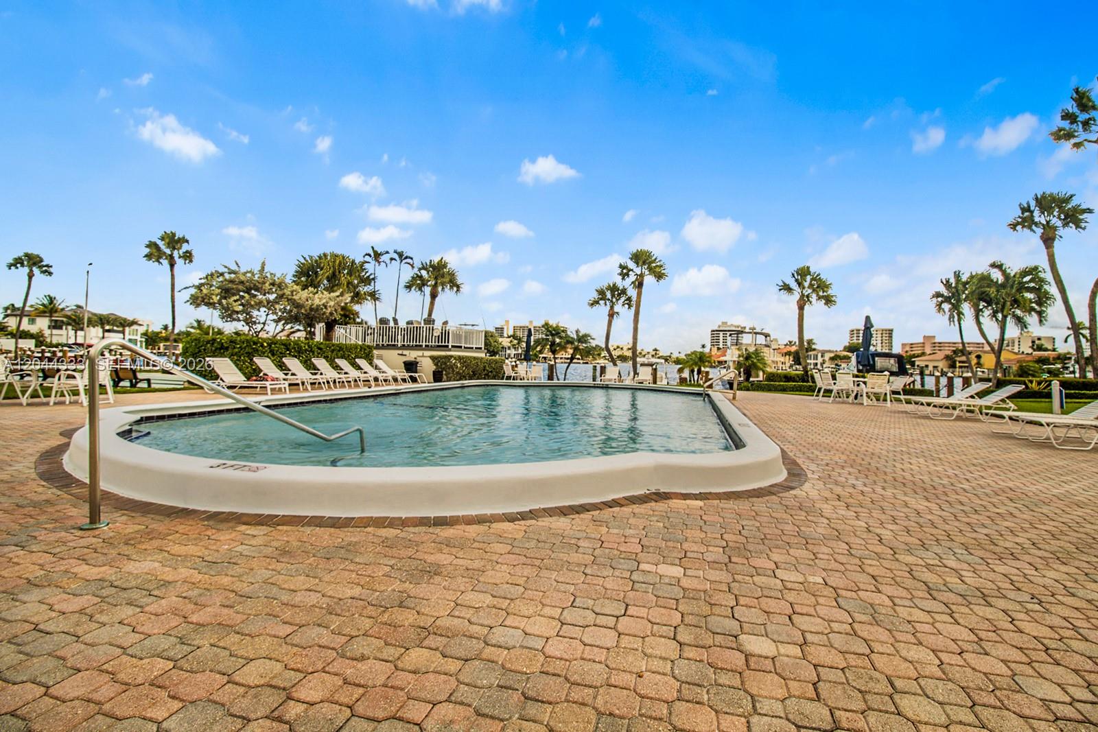 A swimming pool with a metal handrail sits on a brick patio near palm trees — 3401 Spanish Trl # 454, Delray Beach FL 33483, DELRAY BEACH, FL