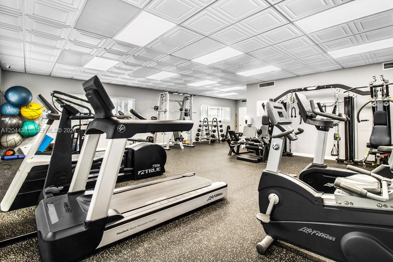 This gym features various exercise machines, rubber flooring, and a drop ceiling with recessed lighting — 3401 Spanish Trl # 454, Delray Beach FL 33483, DELRAY BEACH, FL