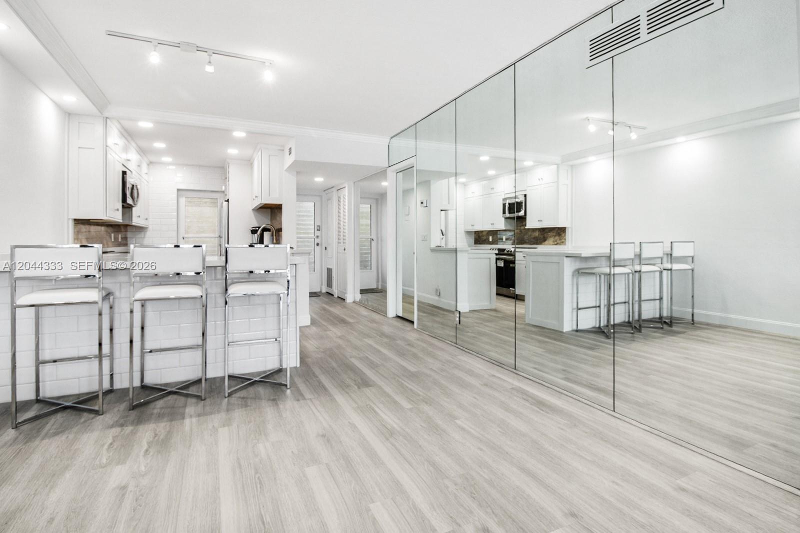 A kitchen features white cabinetry, a breakfast bar with three stools, and a mirrored wall — 3401 Spanish Trl # 454, Delray Beach FL 33483, DELRAY BEACH, FL