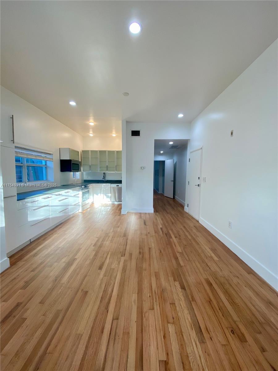 A kitchen with white cabinets and stainless steel appliances opens into a hardwood-floored living area — 929 Michigan Ave # 5, Miami Beach FL 33139, MIAMI BEACH, FL