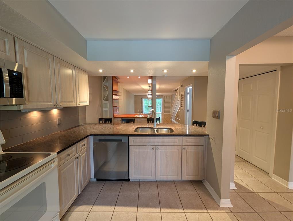 A kitchen features light wood cabinets, dark granite countertops, stainless steel appliances, and tile flooring — 2577 DOLLY BAY DRIVE UNIT 302, PALM HARBOR, FL