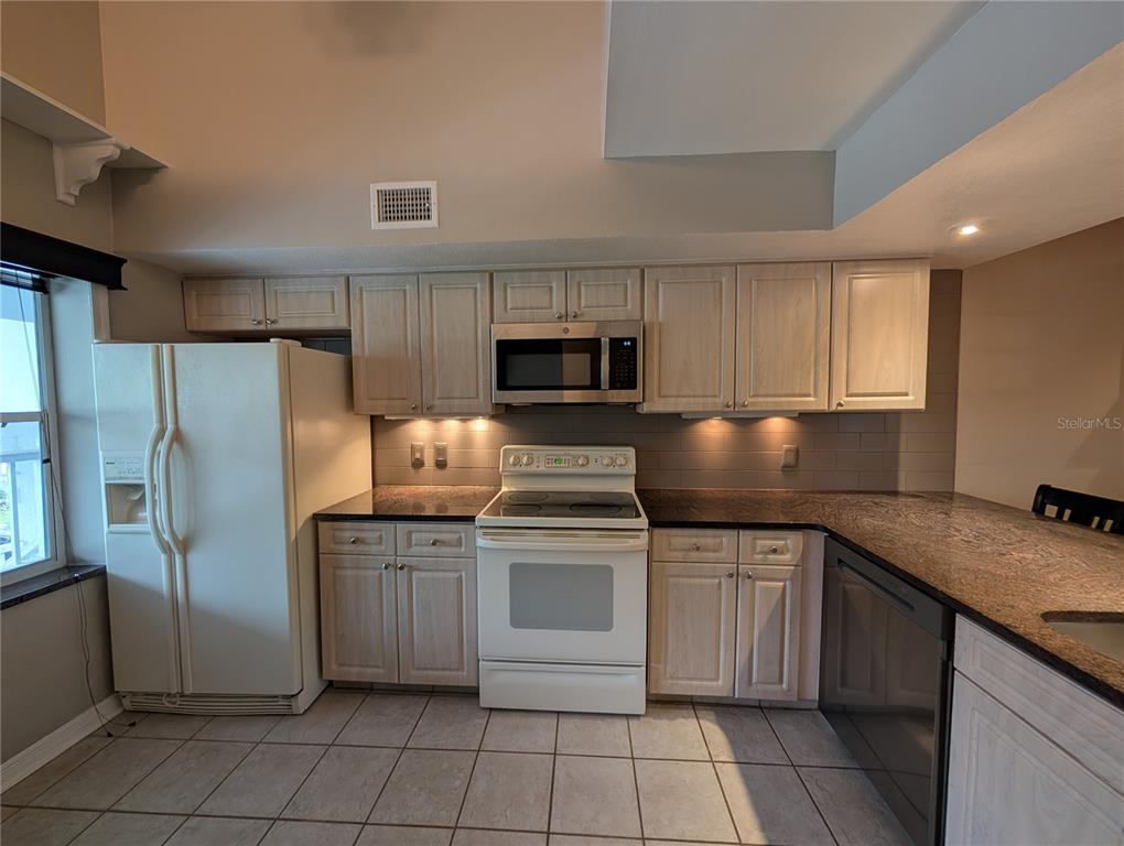 A kitchen features light wood cabinets, white appliances, dark granite countertops, and tiled flooring — 2577 DOLLY BAY DRIVE UNIT 302, PALM HARBOR, FL