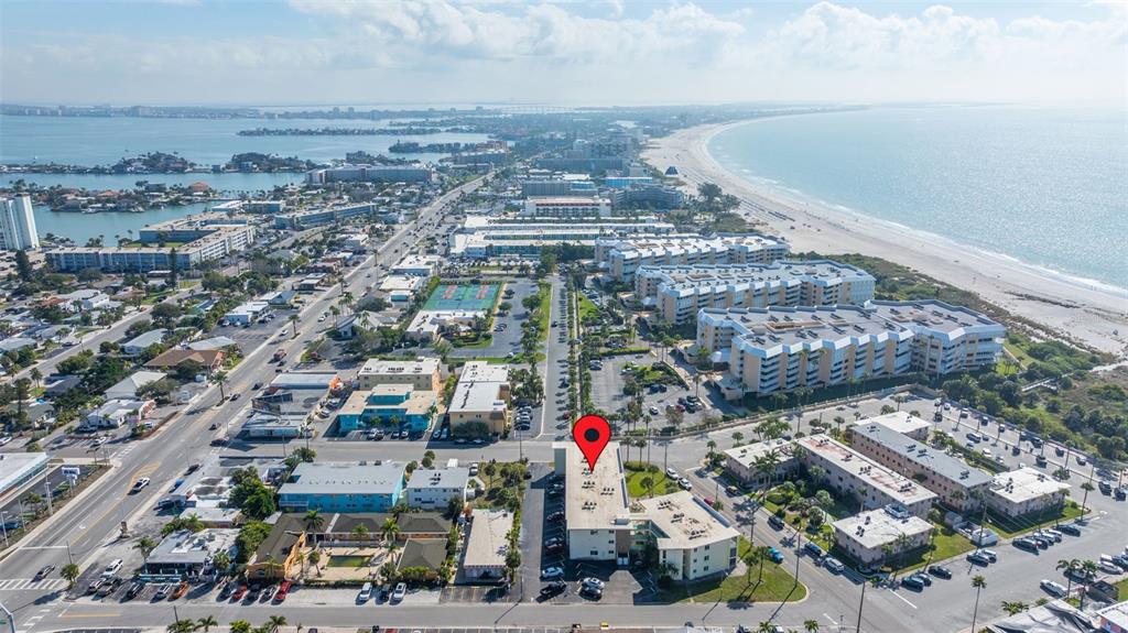 An aerial view shows a coastal town with multi-story apartment buildings near the beach — 6767 SUNSET WAY UNIT 206, ST PETE BEACH, FL