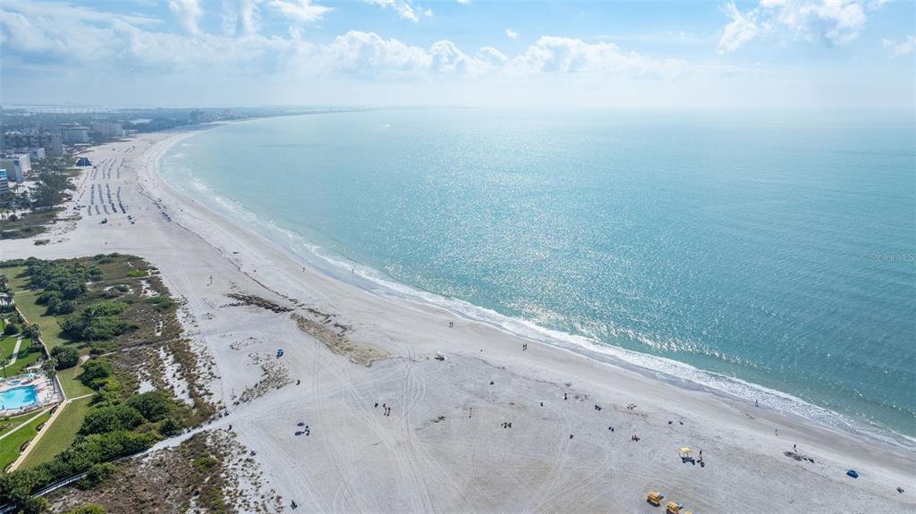 An aerial view shows a sandy beach along the ocean with nearby resort buildings — 6767 SUNSET WAY UNIT 206, ST PETE BEACH, FL