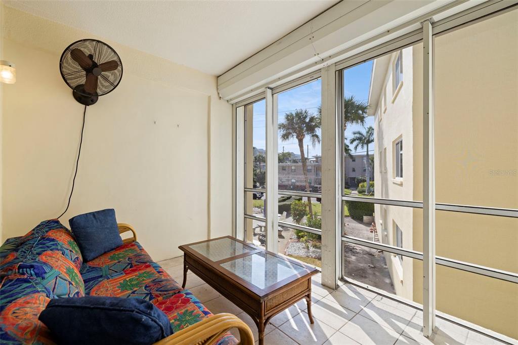 A sunroom features a patterned sofa, a glass-top coffee table, and large windows — 6767 SUNSET WAY UNIT 206, ST PETE BEACH, FL