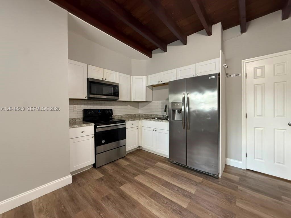 A kitchen features white cabinets, stainless steel appliances, and wood-look flooring under exposed ceiling beams — 10335 NW 2nd Ct # 1, Miami FL 33150, MIAMI, FL