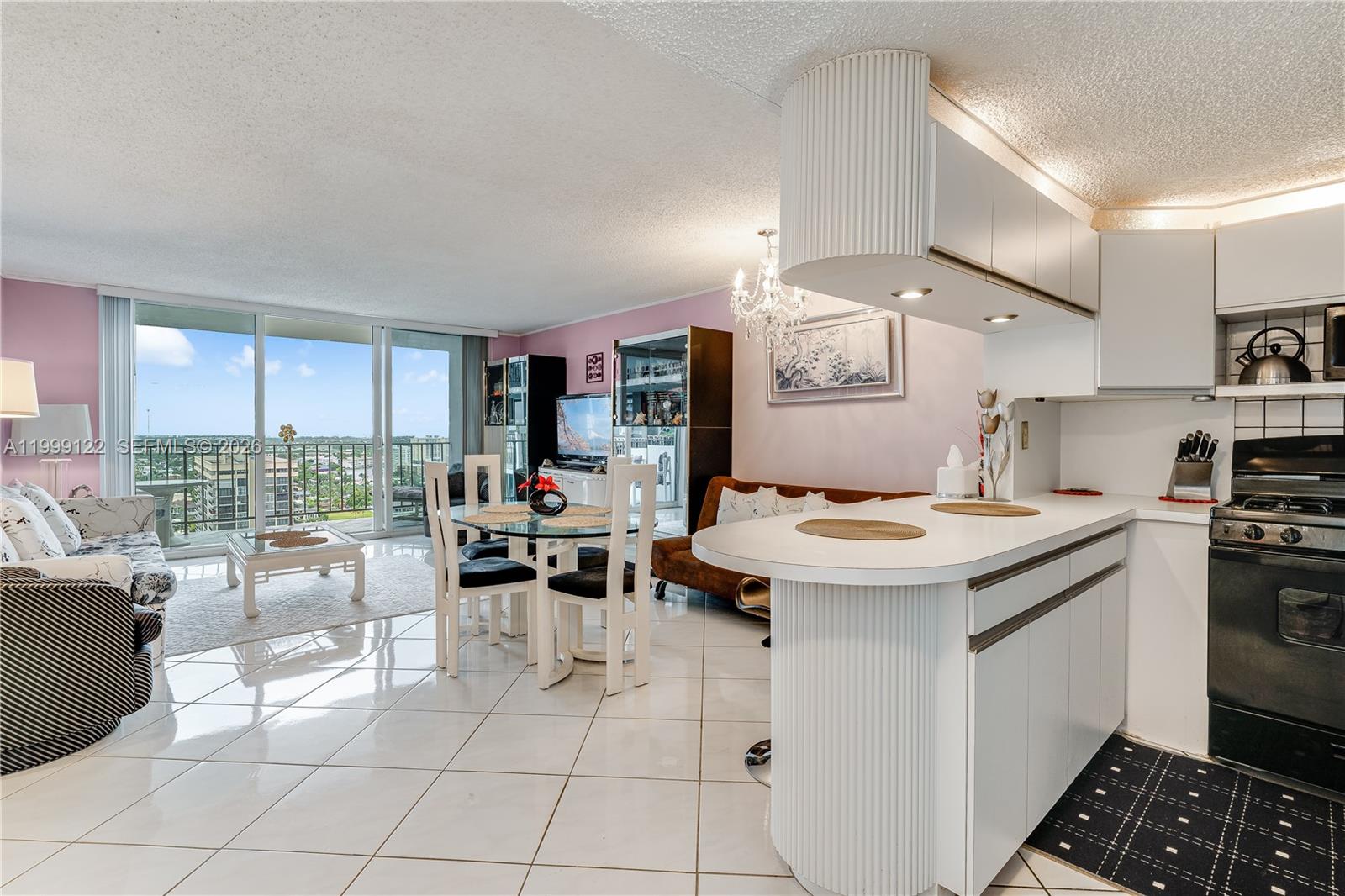 An open-concept living and dining area features white tile floors, a kitchen peninsula, and balcony access — 2030 S Ocean Dr # 1903, Hallandale Beach FL 33009, HALLANDALE BEACH, FL
