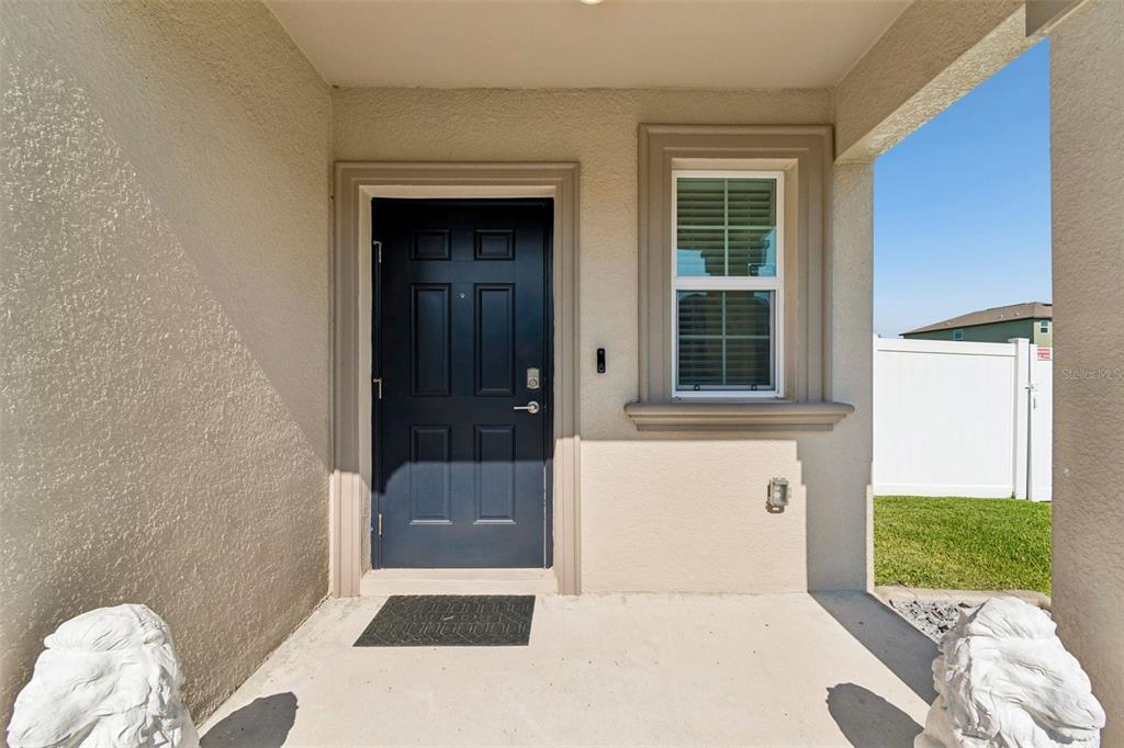 A covered entryway features a dark blue front door, a window, and two lion statues — 6450 BACK FORTY LOOP, ZEPHYRHILLS, FL