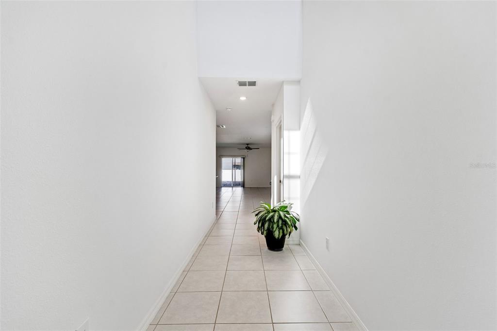A tiled hallway leads from a high-ceilinged entryway toward a bright living area — 6450 BACK FORTY LOOP, ZEPHYRHILLS, FL