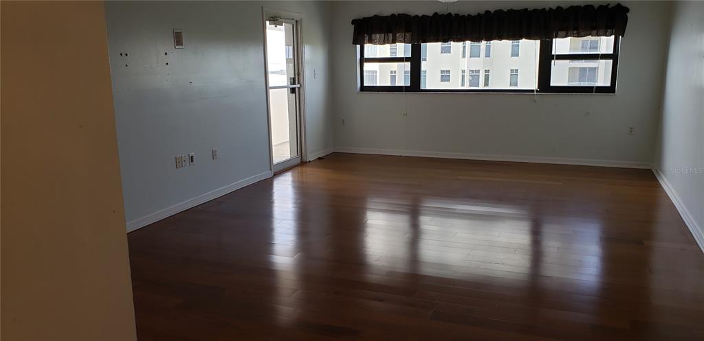 An empty room features hardwood flooring, a glass door, and a large window with blinds — 4141 BAYSHORE BOULEVARD S UNIT 1502, TAMPA, FL