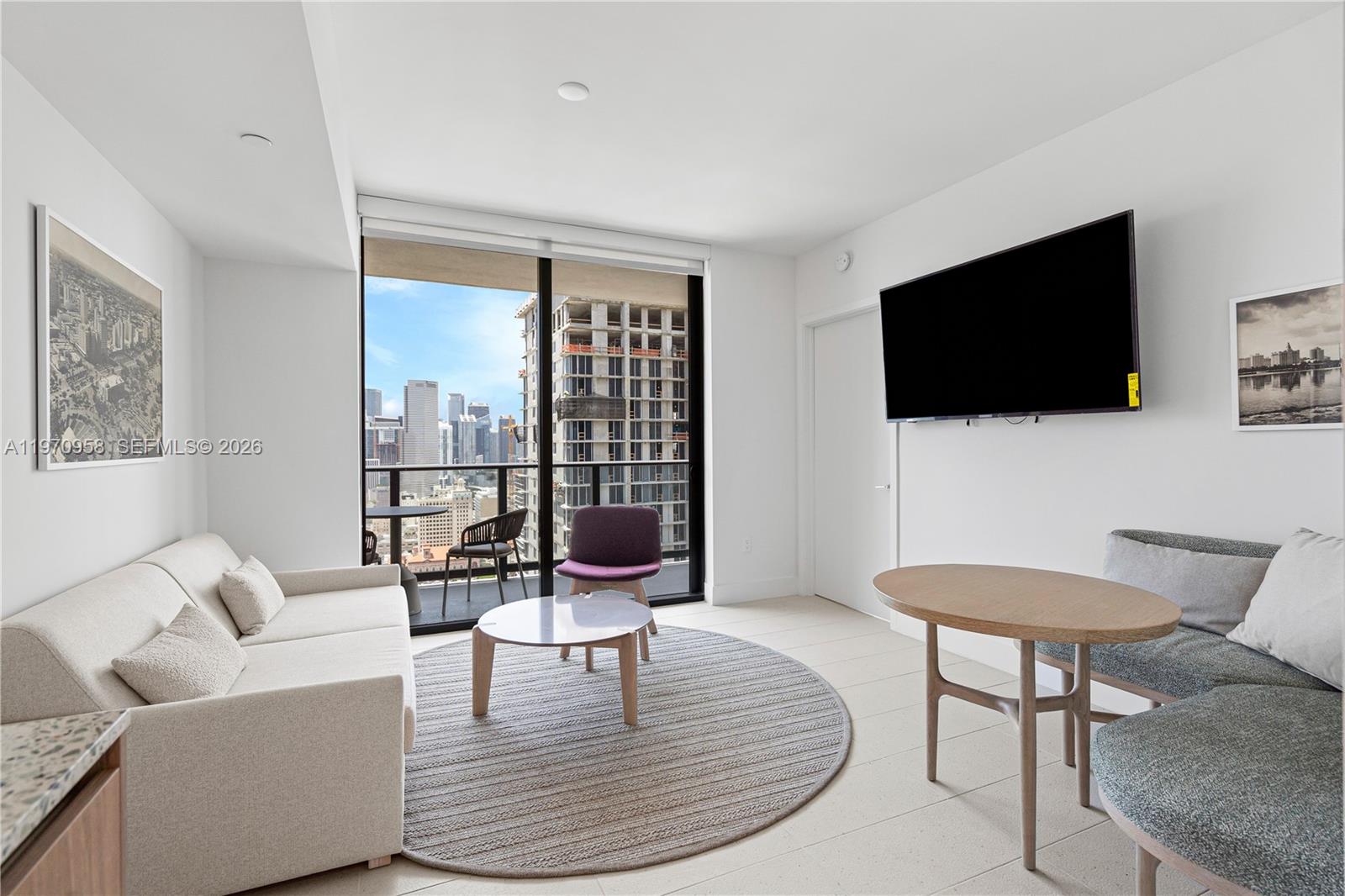 A modern living room features a sofa, round rug, dining table, and a city balcony view — 159 NE 6th St # 2707, Miami FL 33132, MIAMI, FL