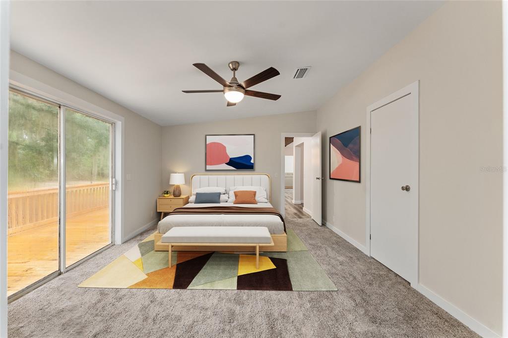 A bedroom features a bed, a geometric rug, a ceiling fan, and a sliding glass door — 6028 SW 91ST PLACE, LAKE BUTLER, FL