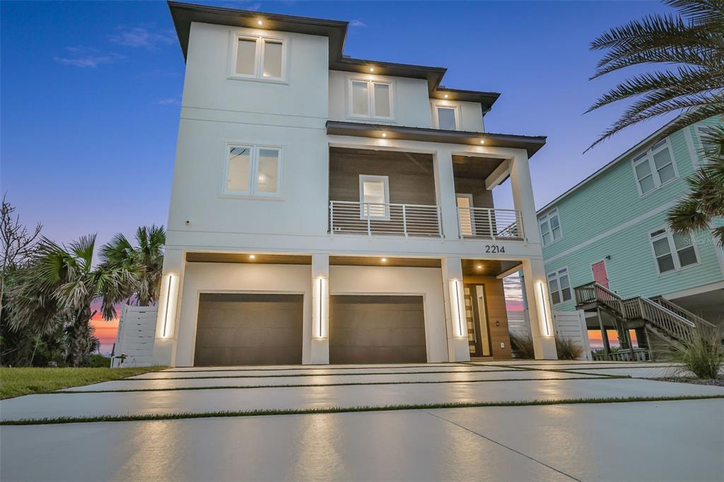 A three-story modern house with a two-car garage and a covered balcony at dusk — 2214 N CENTRAL AVENUE, FLAGLER BEACH, FL
