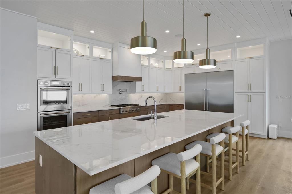 A modern kitchen features a large marble-topped island, white cabinetry, wood accents, and pendant lighting — 2214 N CENTRAL AVENUE, FLAGLER BEACH, FL
