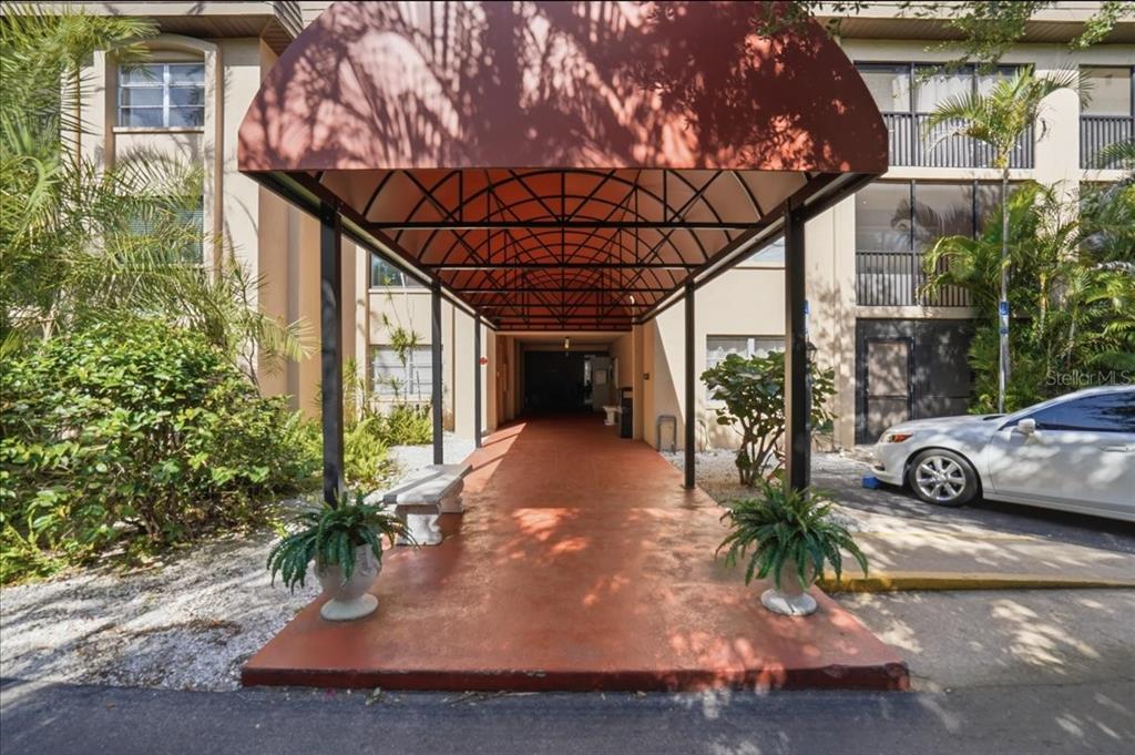 A covered walkway with a red awning leads to the entrance of a multi-story building — 3700 S OSPREY AVENUE UNIT 115, SARASOTA, FL