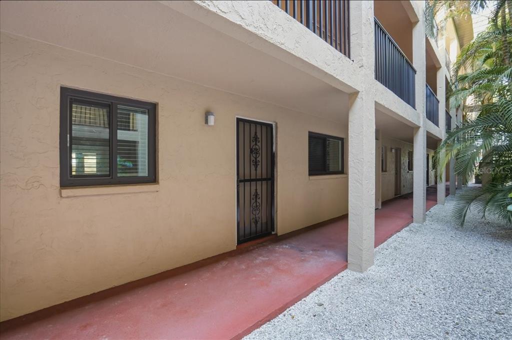 A ground-level apartment entrance with a screen door and windows along a covered walkway — 3700 S OSPREY AVENUE UNIT 115, SARASOTA, FL