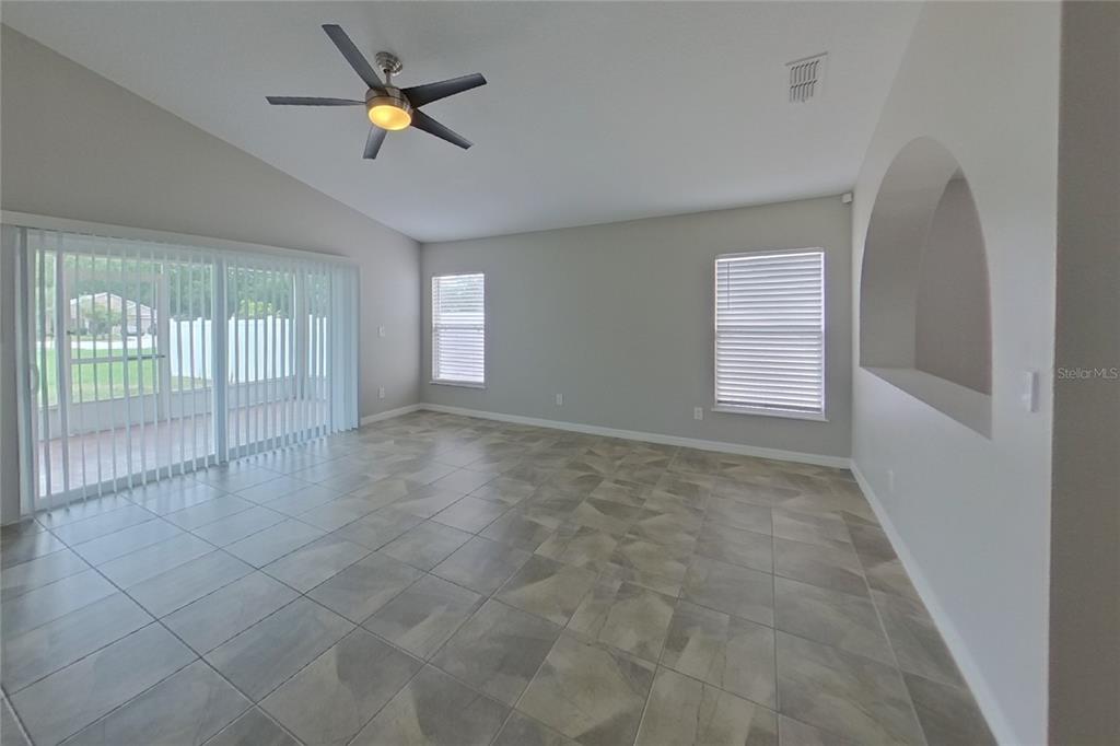 A living room with tile flooring, a ceiling fan, sliding glass doors, and arched wall cutout — 302 ANORAK STREET, GROVELAND, FL