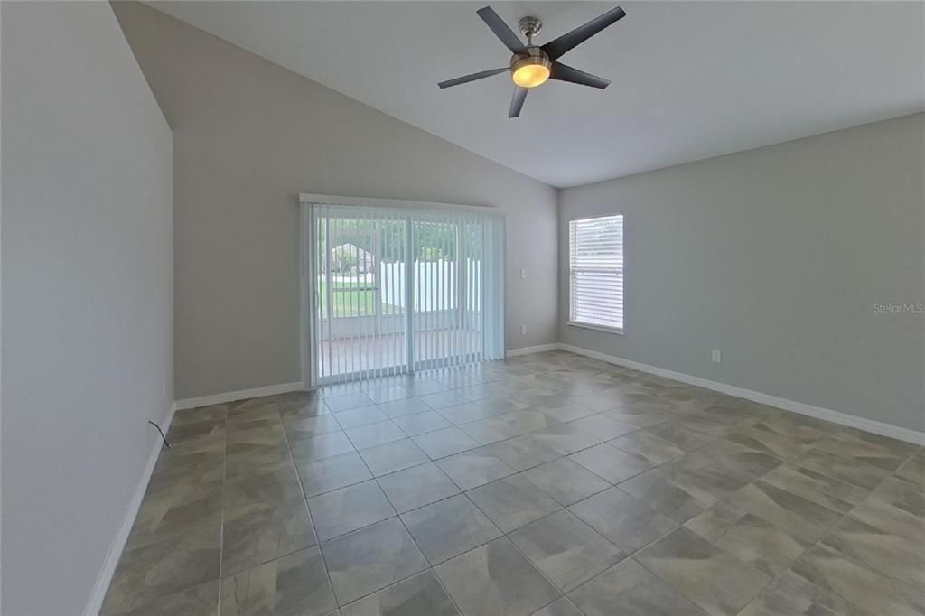 A living room with vaulted ceilings, tile flooring, a ceiling fan, and sliding glass doors — 302 ANORAK STREET, GROVELAND, FL