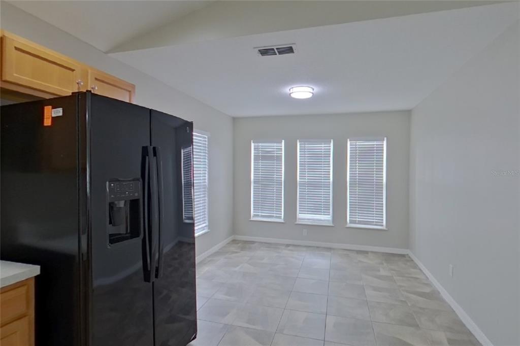 A kitchen dining area features light tile flooring, a black refrigerator, and three large windows — 302 ANORAK STREET, GROVELAND, FL