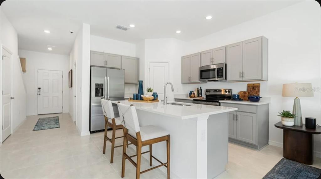 A modern kitchen features gray cabinets, stainless steel appliances, and a white quartz island — 7187 GRAND FOREST WAY, NOKOMIS, FL