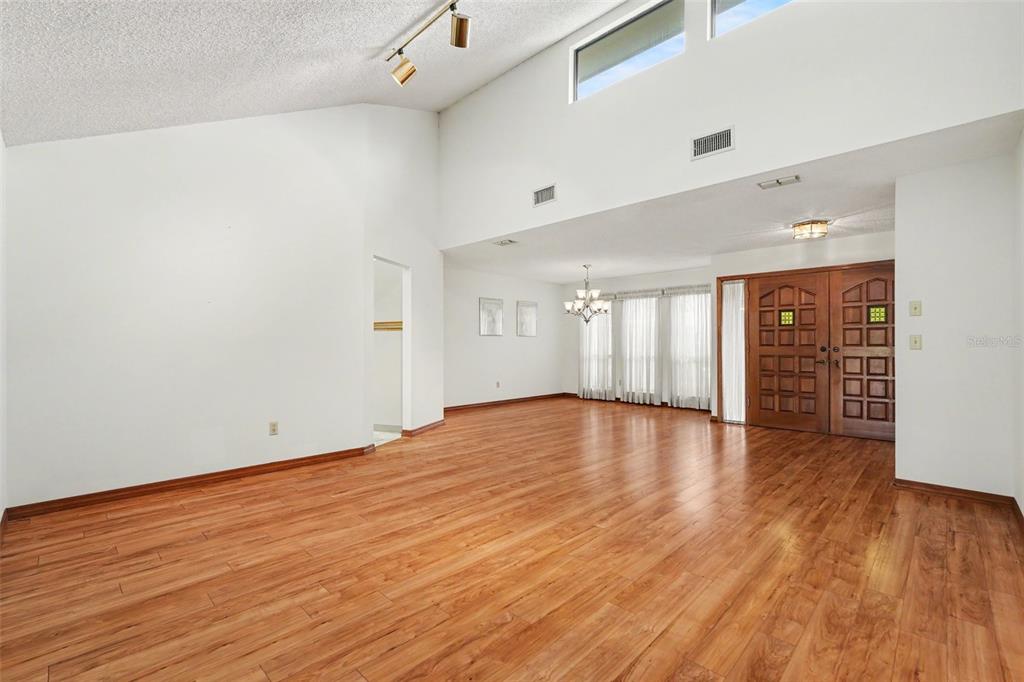 A spacious living room features vaulted ceilings, wood-look flooring, and double front entry doors — 34334 WHISPERING OAKS BOULEVARD, DADE CITY, FL