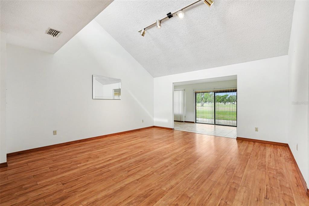 A living room with vaulted ceilings, wood-look flooring, track lighting, and a sliding glass door — 34334 WHISPERING OAKS BOULEVARD, DADE CITY, FL