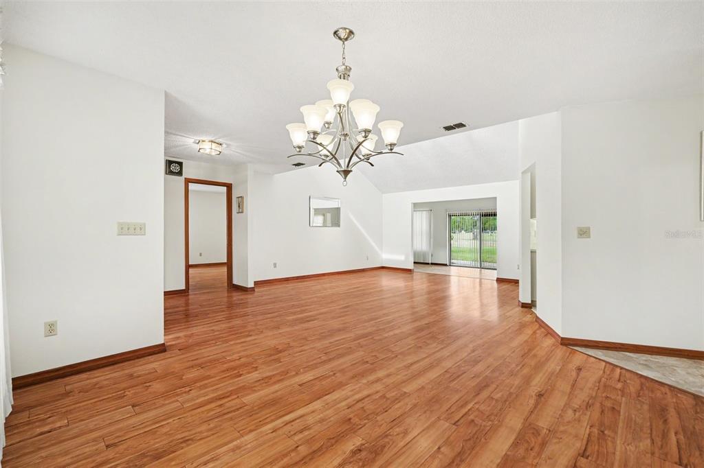 An empty living room features wood-look flooring, a vaulted ceiling, and a large chandelier — 34334 WHISPERING OAKS BOULEVARD, DADE CITY, FL