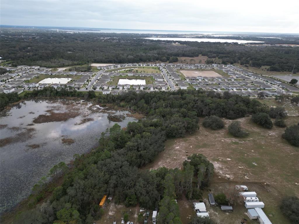 An aerial view shows a residential subdivision adjacent to a large pond and wooded area — 9915 COUNTY ROAD 44, LEESBURG, FL