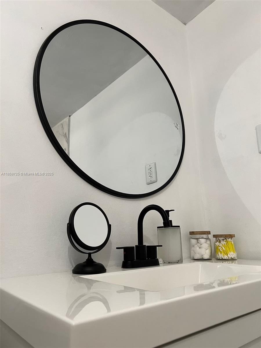 A bathroom vanity features a white sink, black faucet, round mirror, and countertop accessories — 2701 NW 24th Ct # R, Miami FL 33142, MIAMI, FL