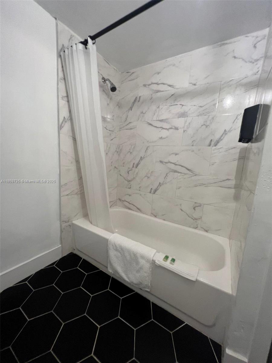 A bathroom features a white bathtub, marble-patterned wall tiles, and black hexagonal floor tiles — 2701 NW 24th Ct # R, Miami FL 33142, MIAMI, FL