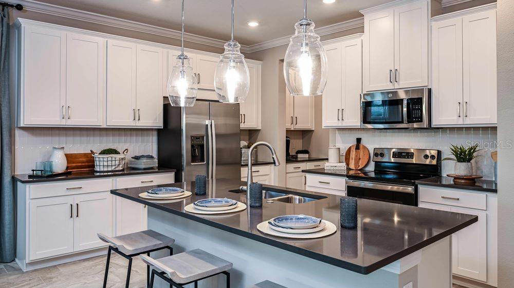 A modern kitchen features white cabinetry, dark countertops, a central island, and stainless steel appliances — 6929 PRAIRIE OAK WAY, NOKOMIS, FL