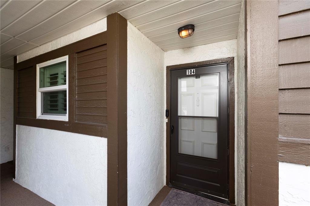 The exterior entrance of a residence features a brown door numbered 104 and a window — 4008 PASSPORT LANE UNIT 104, NEW PORT RICHEY, FL